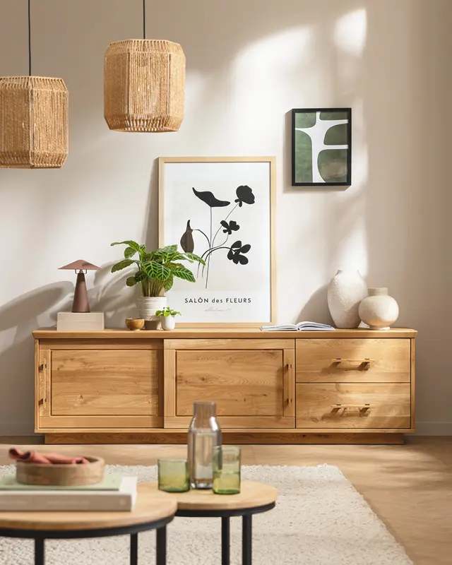 Holzsideboard mit Bildern, Pflanzen, Vasen und zwei Hängeleuchten an heller Wand